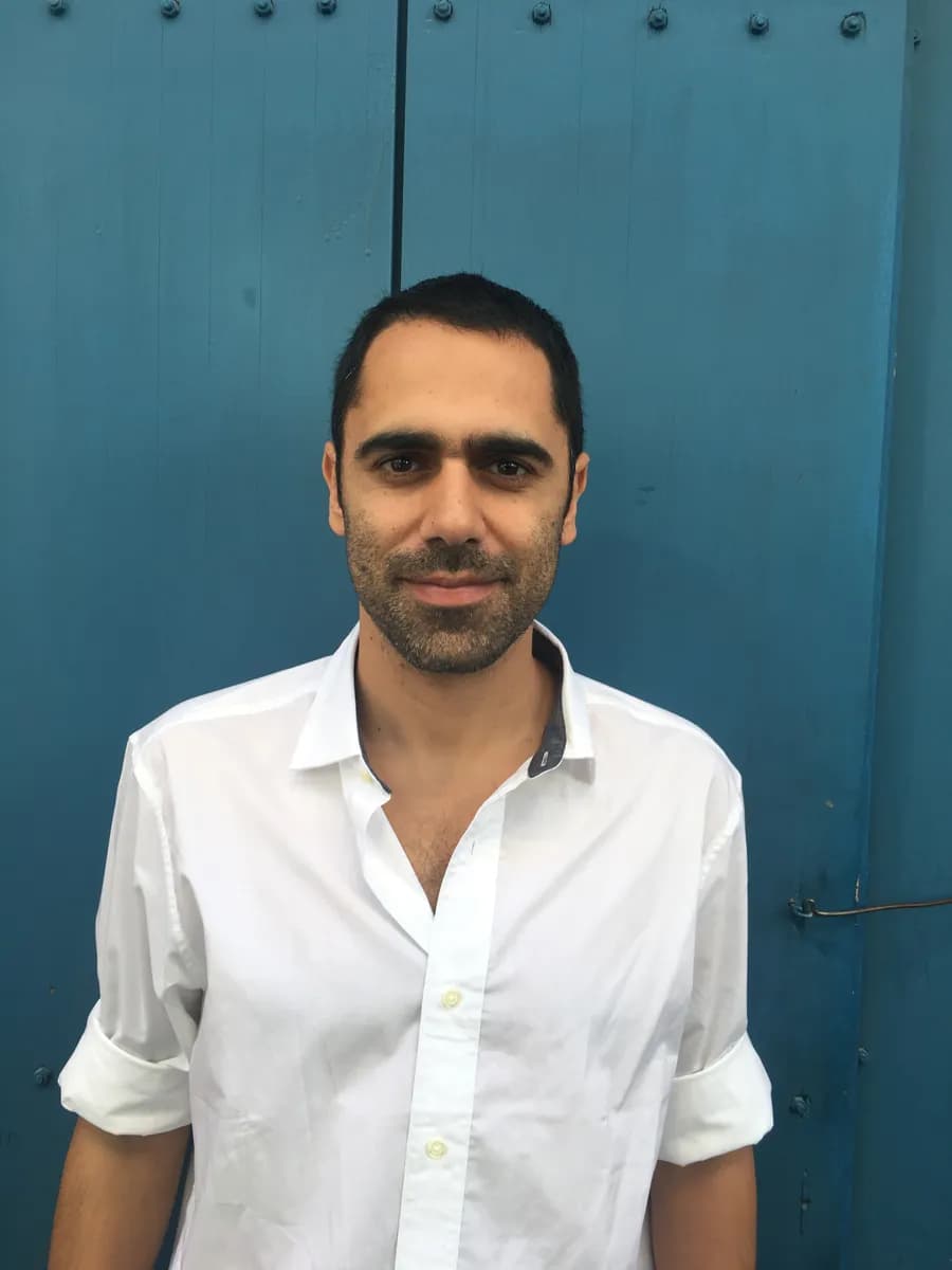 Sinay Elihay in a white shirt, standing in front of a blue wooden door