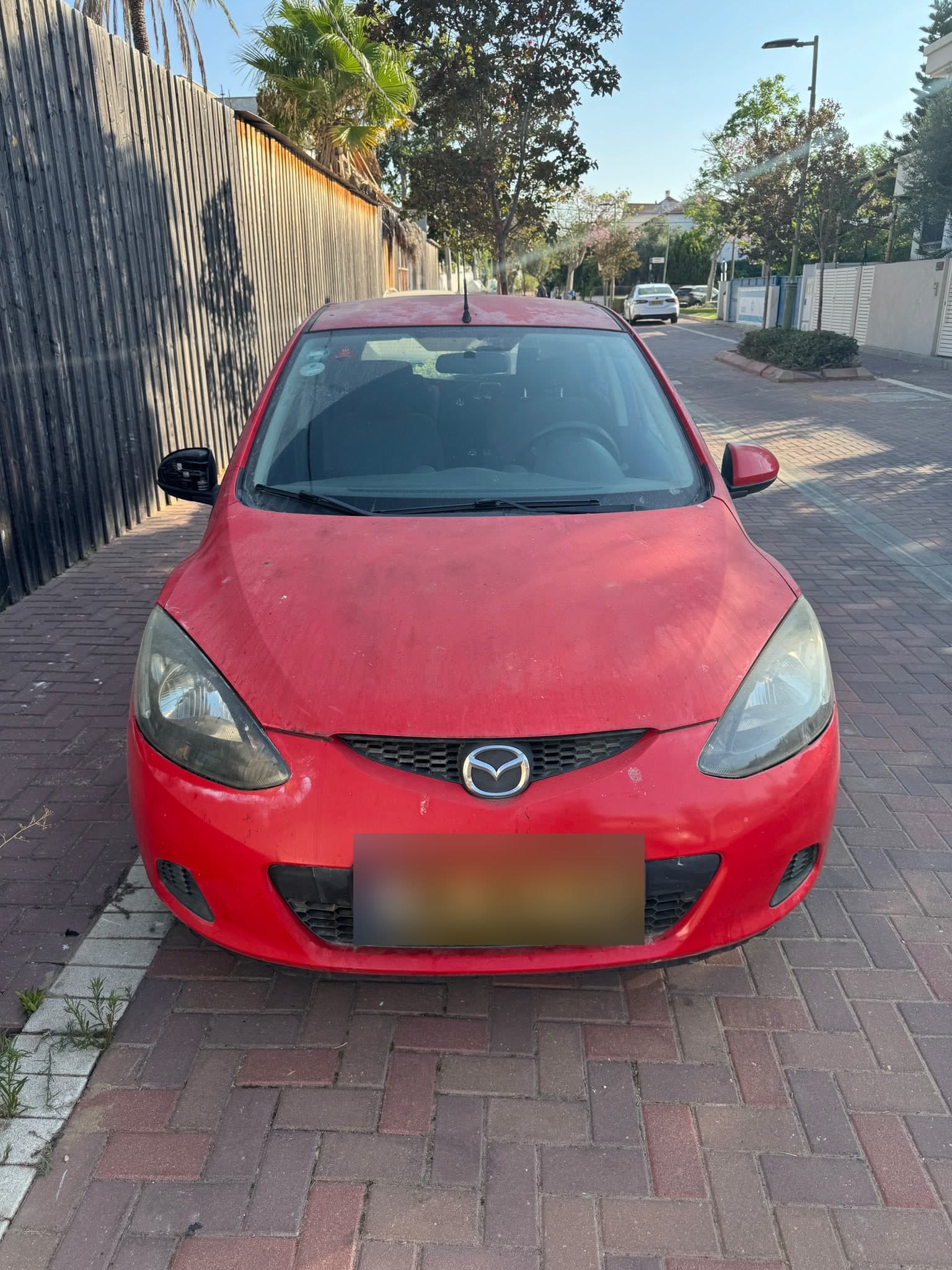 The red Mazda 2 parked on a brick sidewalk, the original listing photo